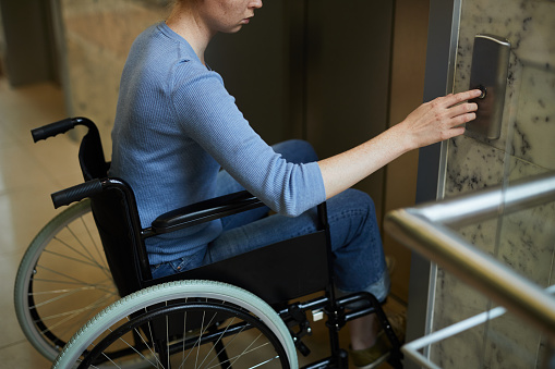 Close-up of young disabled female patient in wheelchair pushing the button and using the elevator