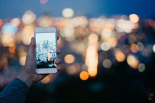 Holding a mobile phone in front of the the city at night