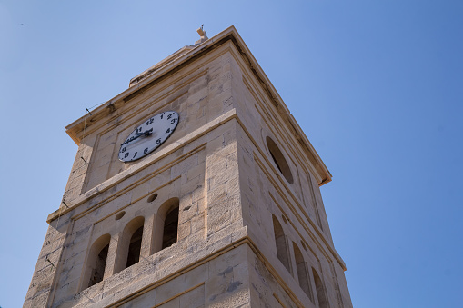 Building of church of Saint George, made of stone. Tower with belfry and clock. Summer blue sky. Primosten, Croatia.