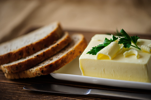 piece of butter with knife, bread and parsley on a wooden desk