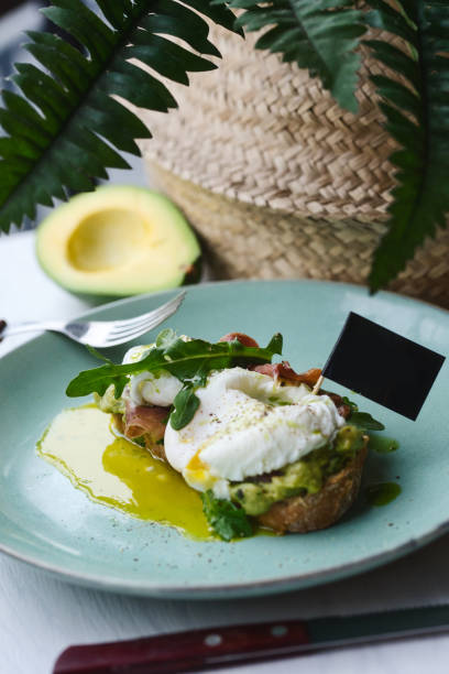 istock Hot toast with jamon, poached egg, herbs and avocado on a plate with a black copy space flag on a skewer 1169008433