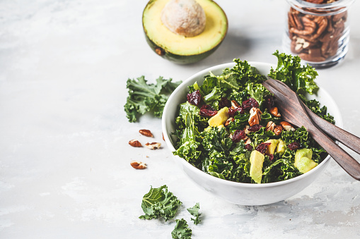 Green kale salad with cranberries and avocado in a white bowl, copy space. Healthy vegan food concept.