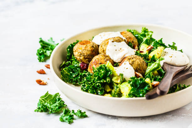 almôndegas vegan das lentilhas com salada verde do kale, abacate e tahini que vestem-se em um prato branco. - produto de carne - fotografias e filmes do acervo