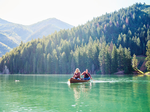 A young adult couple enjoys a canoe ride on a peaceful mountain lake in Utah, United States.