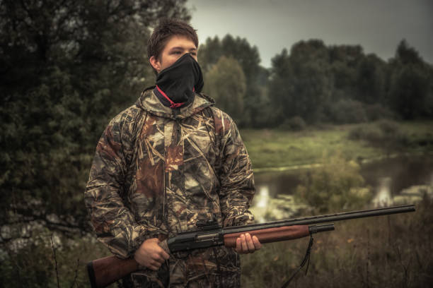 アヒルの狩猟シーズン中にフェイスマスクと銃を持つティーンエイジャーハンター - boyhood ストックフォトと画像