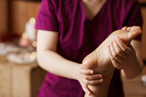 istock Close-up of unrecognizable masseur in uniform twisting ankle of client while making massage in spa salon 1169017596