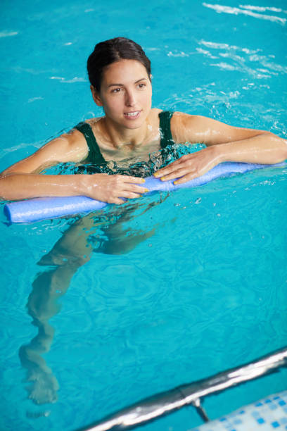 istock Content attractive young brunette woman doing exercise with pool noodle in swimming pool 1169017797