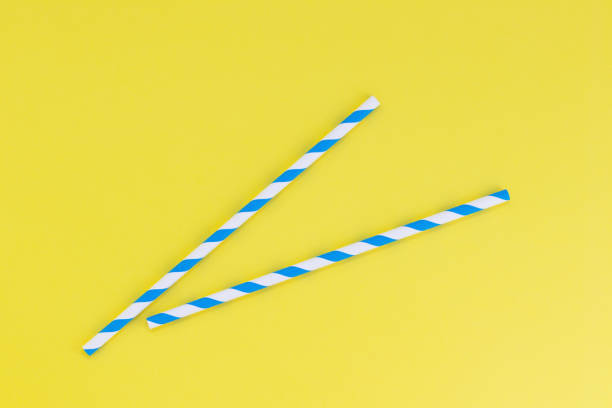 Two blue striped paper straws on a yellow background, with copy space