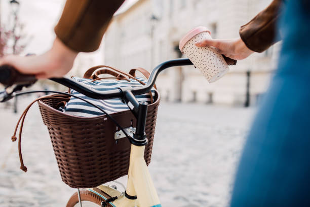 Unrecognizable young woman riding a bicycle and holding a coffee cup on her way to work.