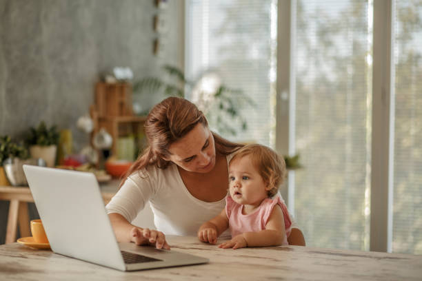 istock Woman cuddling her baby daughter while using laptop 1169041347