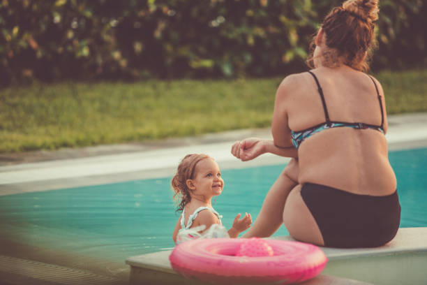 bambina che si rilassa con la madre accanto a una piscina - 12 23 mesi foto e immagini stock