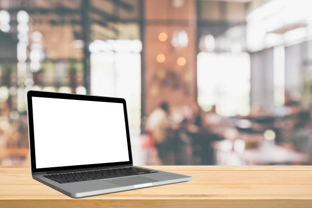istock Blank white screen laptop computer on wood table top with cafe restaurant abstract bokeh light defocused blur background 1169043449
