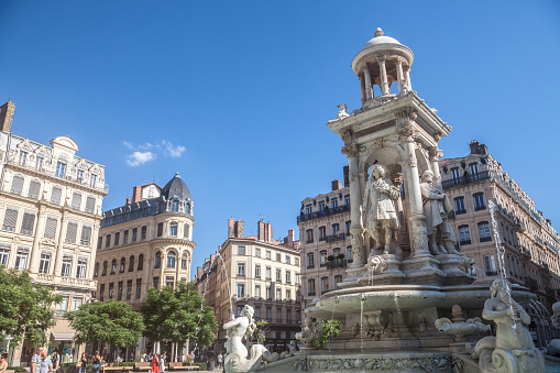 Picture of the fountain of Place des Jacobins square, one of the main landmarks of the city center of Lyon, France, on the Presqu'Ile Peninsula, with pedestrians passing by.