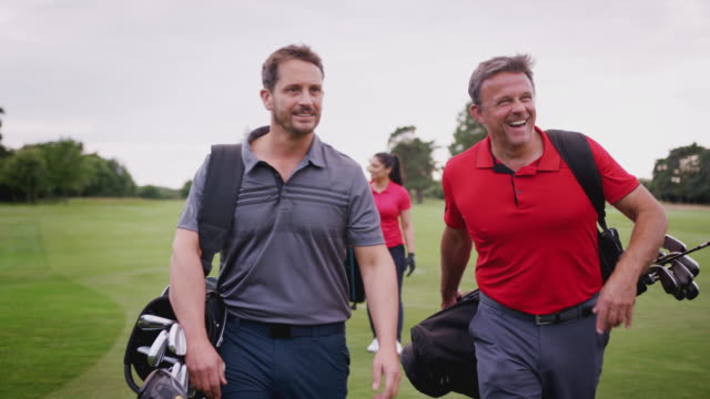 Two Mature Couples Playing Golf Walking Along Fairway Carrying Golf Bag