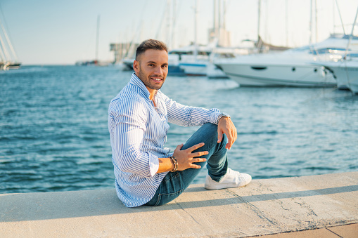 Young rich man at Yacht Club. Businessman is smiling and Relaxing in the gulf with seaview and luxury ships