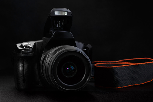 Professional DSLR camera with opened built-in flash on black background. Selective focus