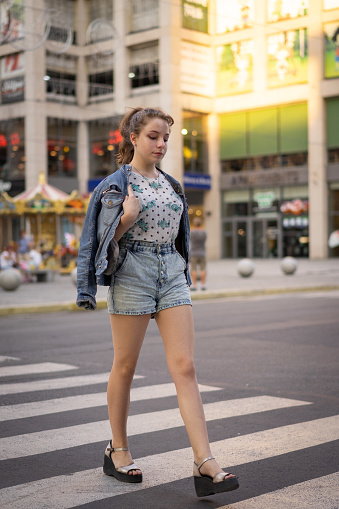 You can see the crosswalk, road and other details of regular urban scene. Girl dressed in a denim shorts, t-shirt and denim jacket. Place on this photo is Katerynoslavs'kyi Blvd, Dnipro city. Main colors are gray, white and blue.