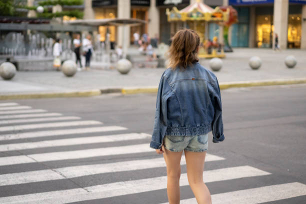 Teenage girl crosses the road. Rear view photo You can see the crosswalk, road and other details of regular urban scene. Girl dressed in a denim shorts, t-shirt and denim jacket. Place on this photo is Katerynoslavs'kyi Blvd, Dnipro city. Main colors are gray, white and blue. Photo was taken from girl's back. dnipropetrovsk stock pictures, royalty-free photos & images