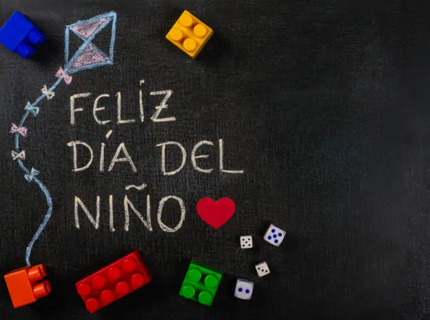 Photo of Blackboard written feliz dia del niño (spanish). Kite design with assembling pieces and game dice. Copy space