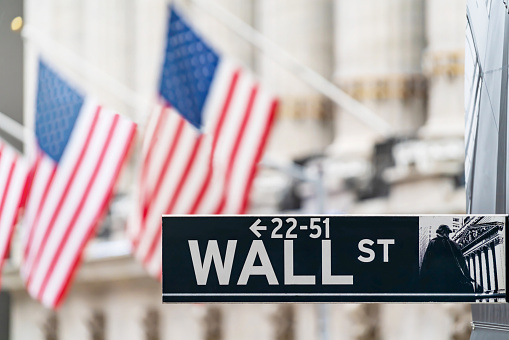 Wall street sign in New York city financial economy and business district with America national flag background. Stock market trade and exchange zone.