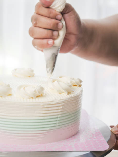 istock Confectioner topping cakes with cream using a pastry bag, 1169078209