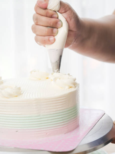 istock Confectioner topping cakes with cream using a pastry bag, 1169078213