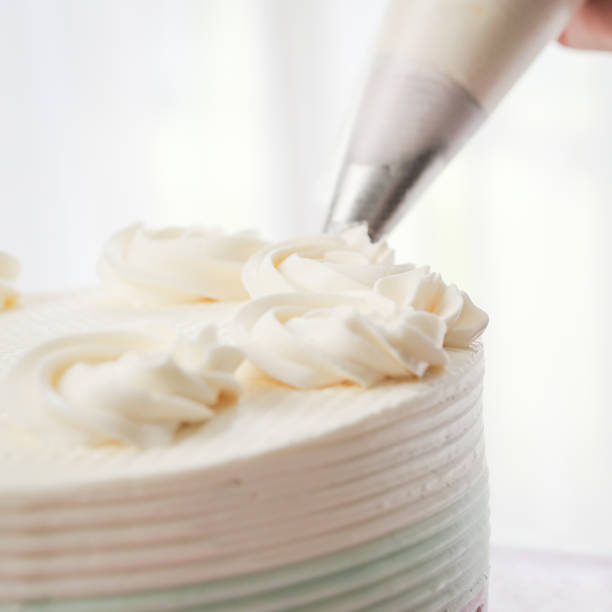 istock Confectioner topping cakes with cream using a pastry bag, 1169078222