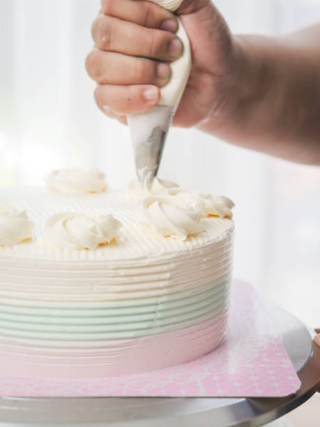 istock Confectioner topping cakes with cream using a pastry bag, 1169078223