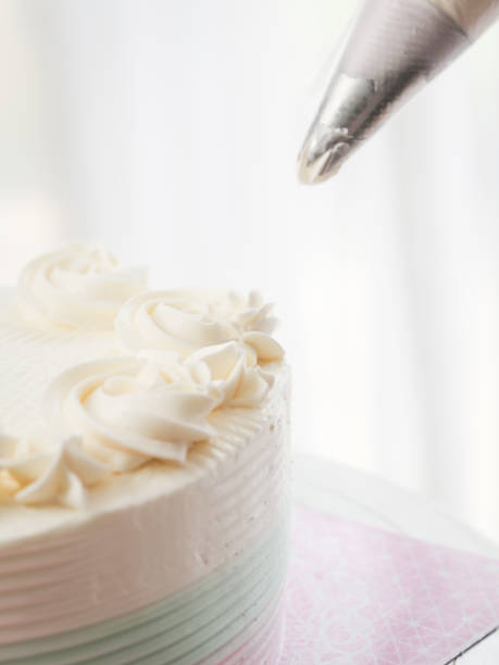 istock Confectioner topping cakes with cream using a pastry bag, 1169078224