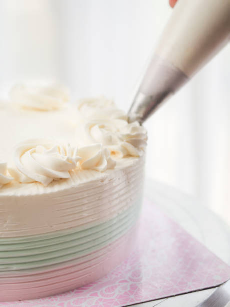 istock Confectioner topping cakes with cream using a pastry bag, 1169078227