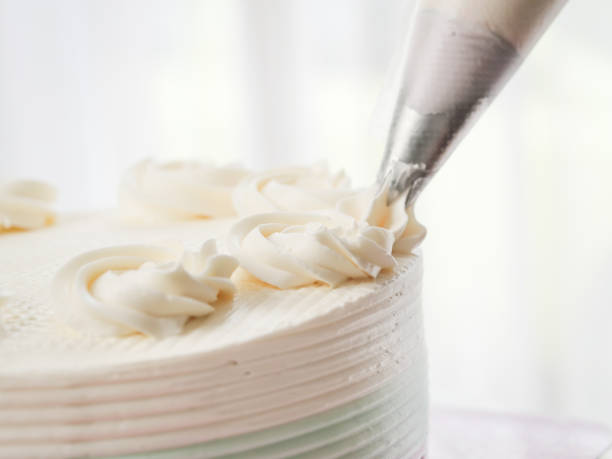 istock Confectioner topping cakes with cream using a pastry bag, 1169078235
