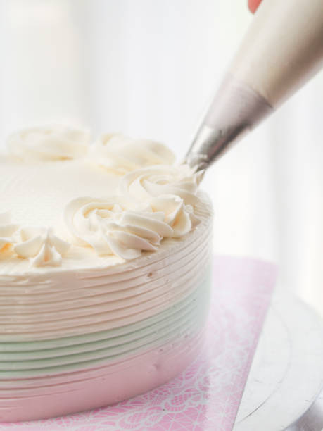 istock Confectioner topping cakes with cream using a pastry bag, 1169078237
