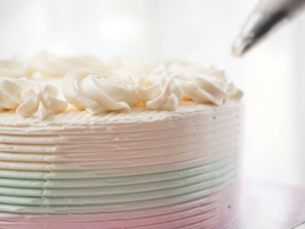 istock Confectioner topping cakes with cream using a pastry bag, 1169078256