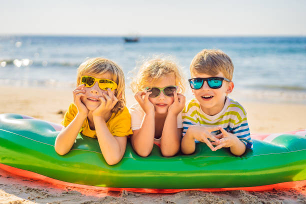 Children sit on an inflatable mattress in sunglasses against the sea and have fun stock photo