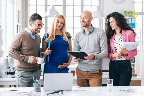 istock Team standing in modern office, talking, pregnant woman 1169080422