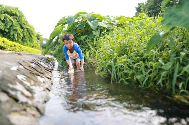 istock Boy plays with toy sailboat in water 1169085646