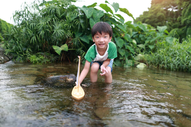istock Boy plays with toy sailboat in water 1169086199