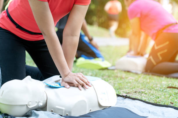 fêmea ou corredor asiático do treinamento da mulher cpr que demonstra a classe no parque põr as mãos e o dedo do intertravamento sobre a boneca do cpr dá a compressão da caixa. treinamento de primeiros socorros para pessoas de ataque cardíaco ou lif - cpr - fotografias e filmes do acervo