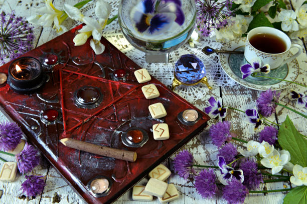 istock Magic book grimoire with runes, flowers, crystals and mystic objects on witch table. 1169093571