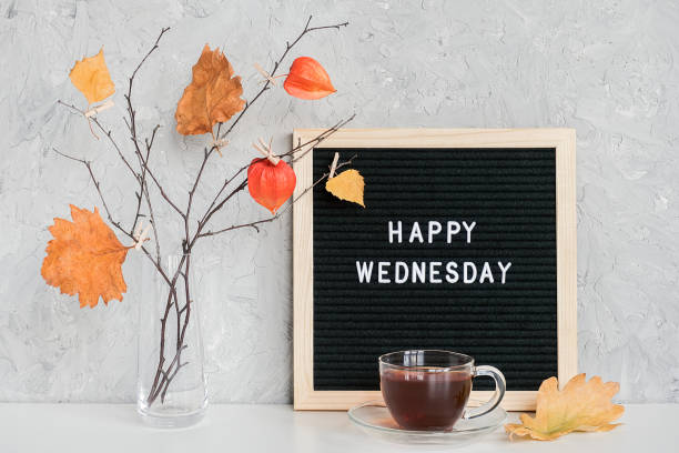 Happy Wednesday text on black letter board and bouquet of branches with yellow leaves on clothespins in vase on table Template for postcard, greeting card Concept Hello autumn Wednesday stock photo