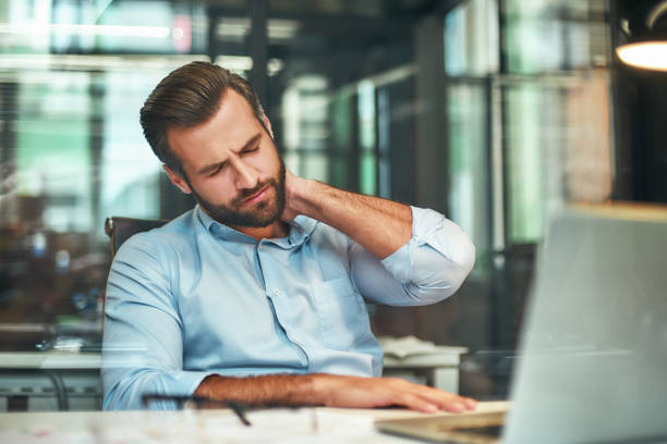 sich müde fühlen. junge bärtige geschäftsmann in formaler kleidung massieren seinen hals, während im modernen büro sitzen - pain backache human spine massaging stock-fotos und bilder