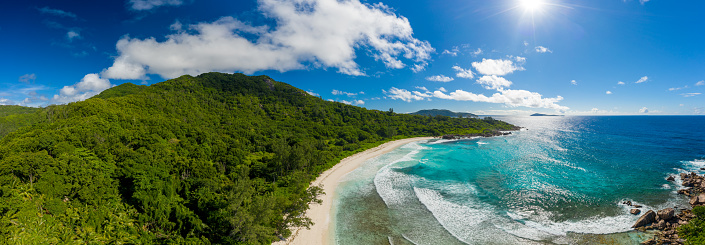 the perfect beach panoramic aerial view of a beach on the island La Digue on Seychelles with beautiful waves and a clear blue sky with some clouds and star shapped sun