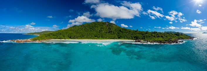 beautiful panoramic aerial view of a beach on the island La Digue on Seychelles with beautiful waves and a clear blue sky with some clouds.