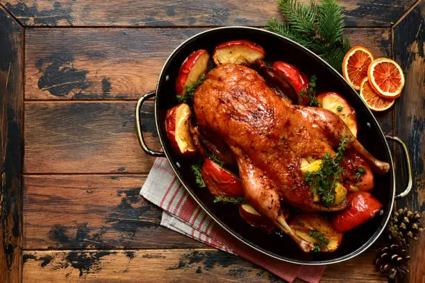 Roast goose stuffed with baked apples in a skillet on a dark wooden background, festive christmas recipe. Top view with copy space.