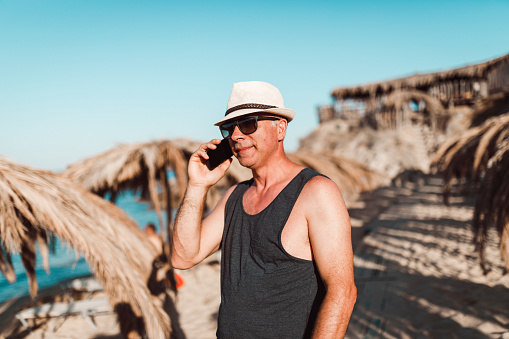 Casual dressed mature man using smart phone at the beach on a sunny summer day