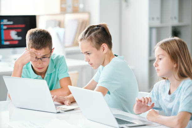 istock Cute schoolchildren sitting by desk in classroom while browsing in the net 1169111073