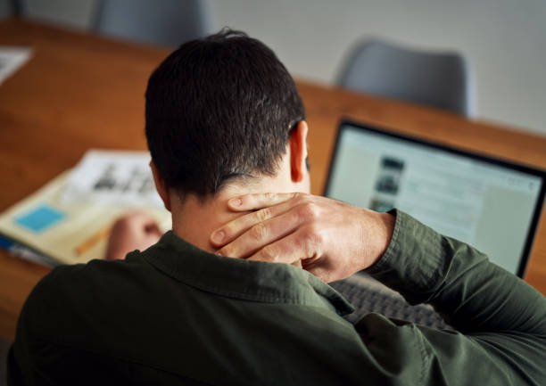 hombre que sufre de dolor de cuello mientras trabaja en la computadora portátil - neck pain fotografías e imágenes de stock