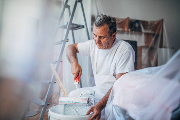 House painter working alone One man, senior man painter in living room, preparing paint with paint roller. house painter ladder paint men stock pictures, royalty-free photos & images