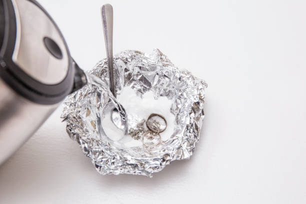 istock A solution of baking soda(Sodium bicarbonate) and warm water will remove the tarnish from silver when the silver is in contact with a piece of aluminium tin foil. Pouring hot water over silver. 1169125757