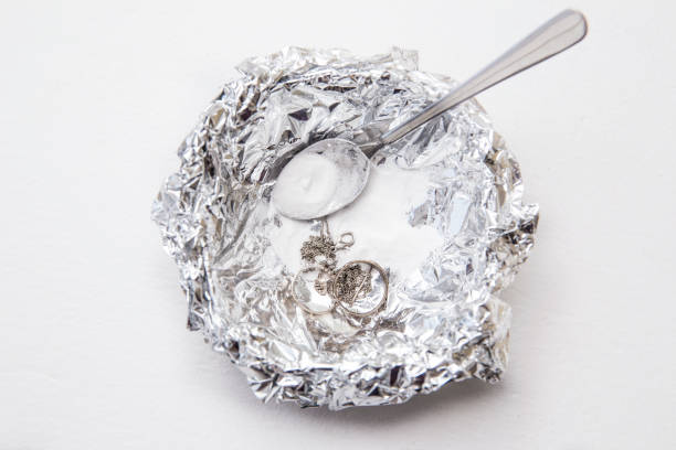 A solution of baking soda(Sodium bicarbonate) and warm water will remove the tarnish from silver when the silver is in contact with a piece of aluminium tin foil. Pouring hot water over silver. stock photo